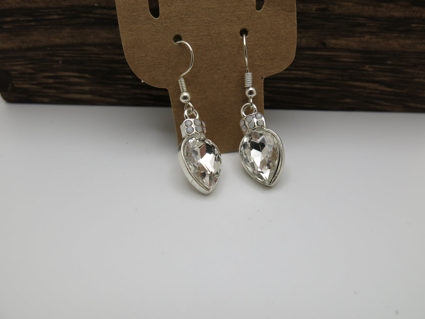 Silver teardrop earrings on a cardboard backing with a wooden surface in the background