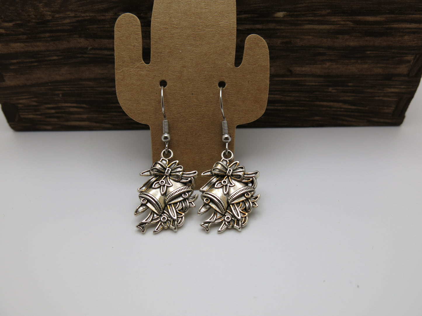 Pair of silver floral earrings on a cactus-shaped earring stand against a wooden background.