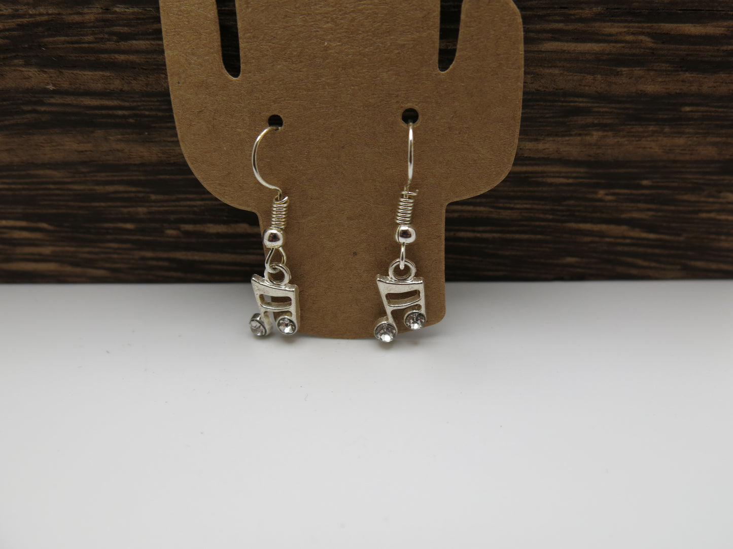Silver note earrings on a cardboard display card against a wooden background
