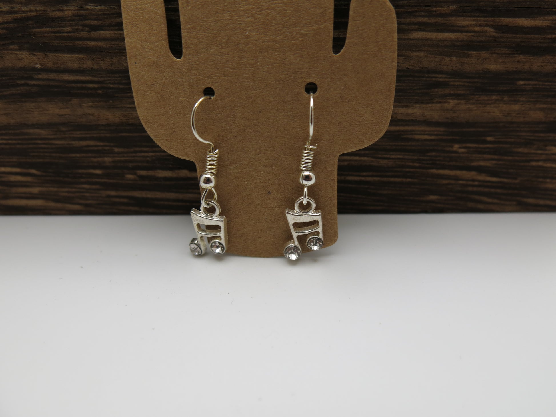 Silver note earrings on a cardboard display card against a wooden background