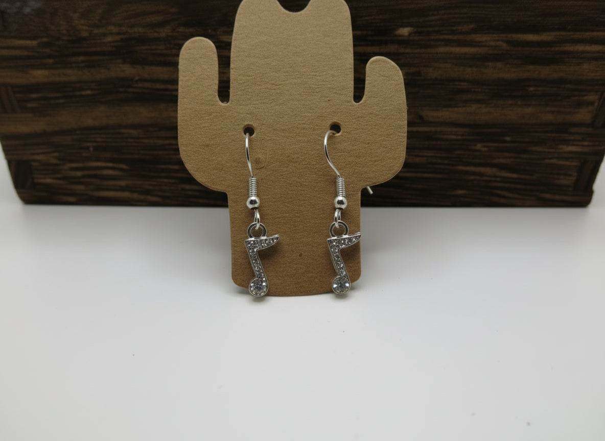 Silver, musical note earrings on a cactus-shaped card against a wooden background