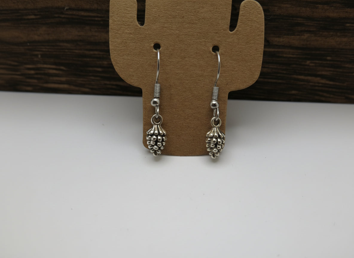 Silver pinecone earrings on a cactus-shaped card with a wooden surface in the background
