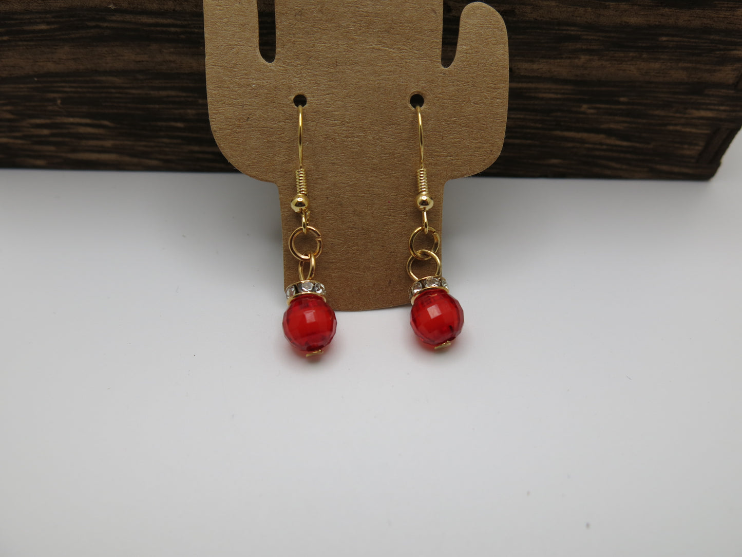 Red earrings with gold hooks on a wooden display card against a white background