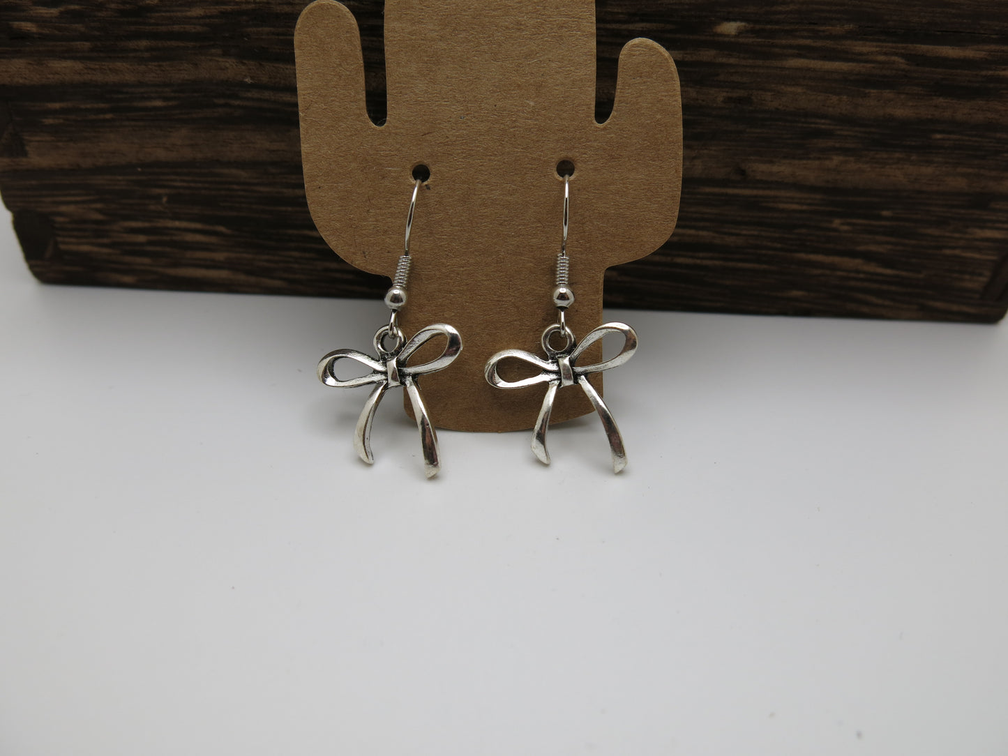 Silver bow-shaped earrings on a cardboard cactus-shaped stand against a wooden background.