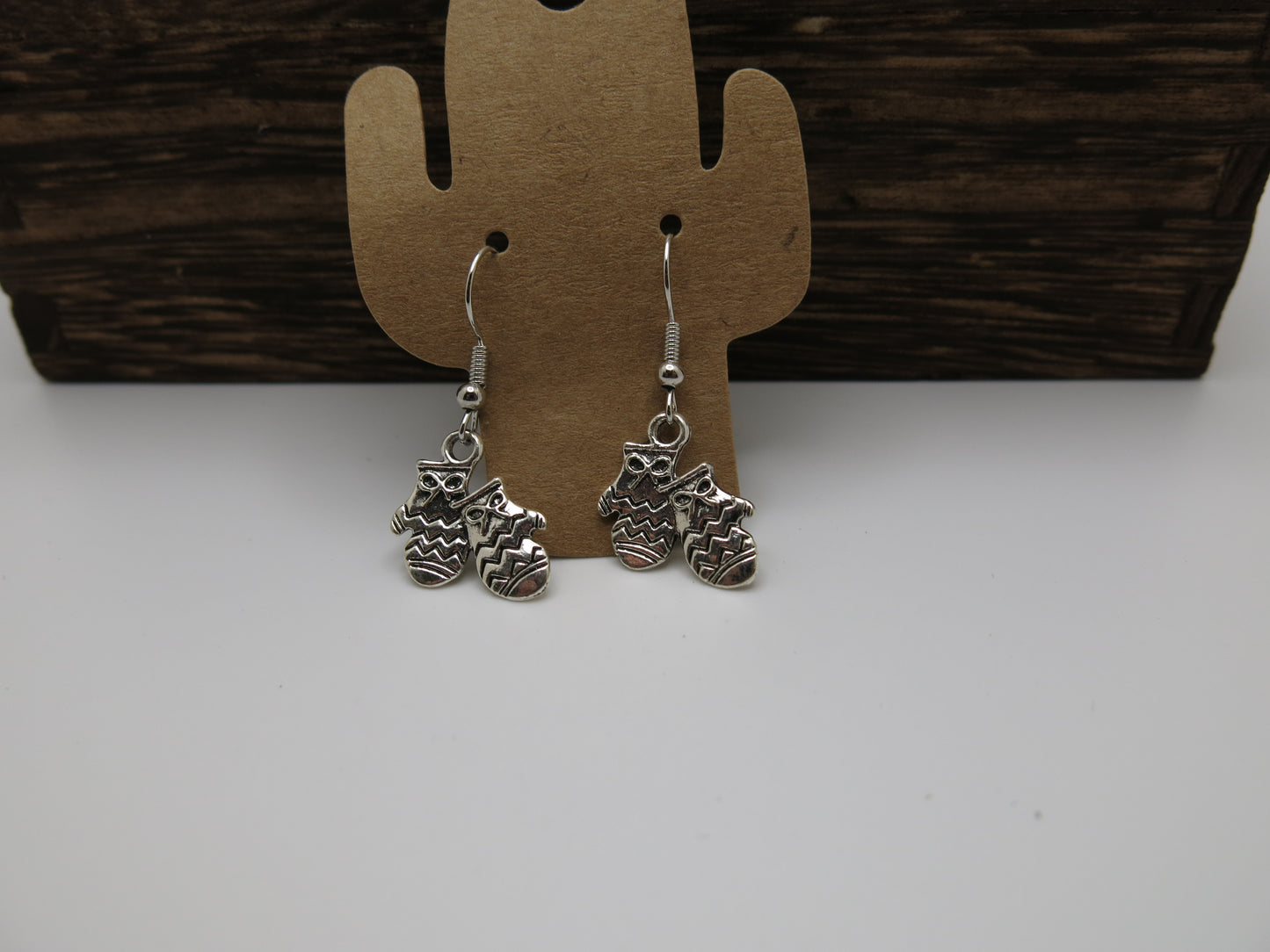 Silver mitten earrings on a cactus-shaped card against a wooden background