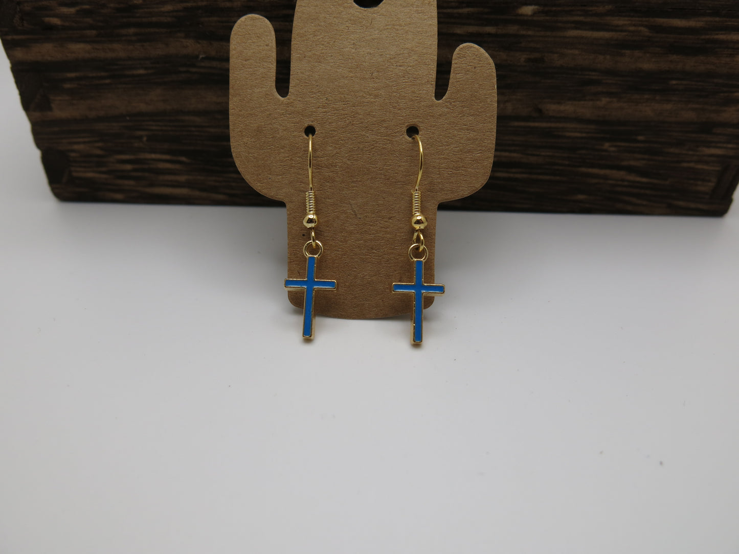 Blue cross earrings on a cactus-shaped earring card with a wooden background