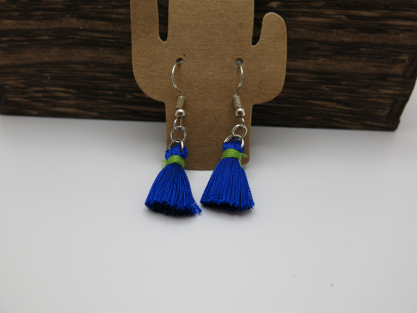Blue tassel earrings on a cardboard cactus-shaped stand against a white background