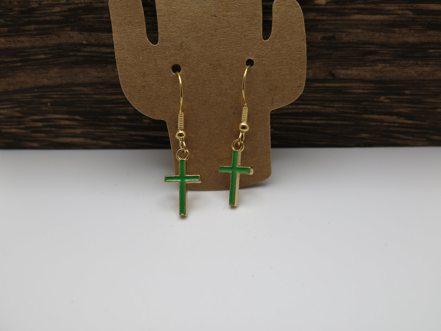 Gold and green cross earrings on a brown earring card with a wooden background