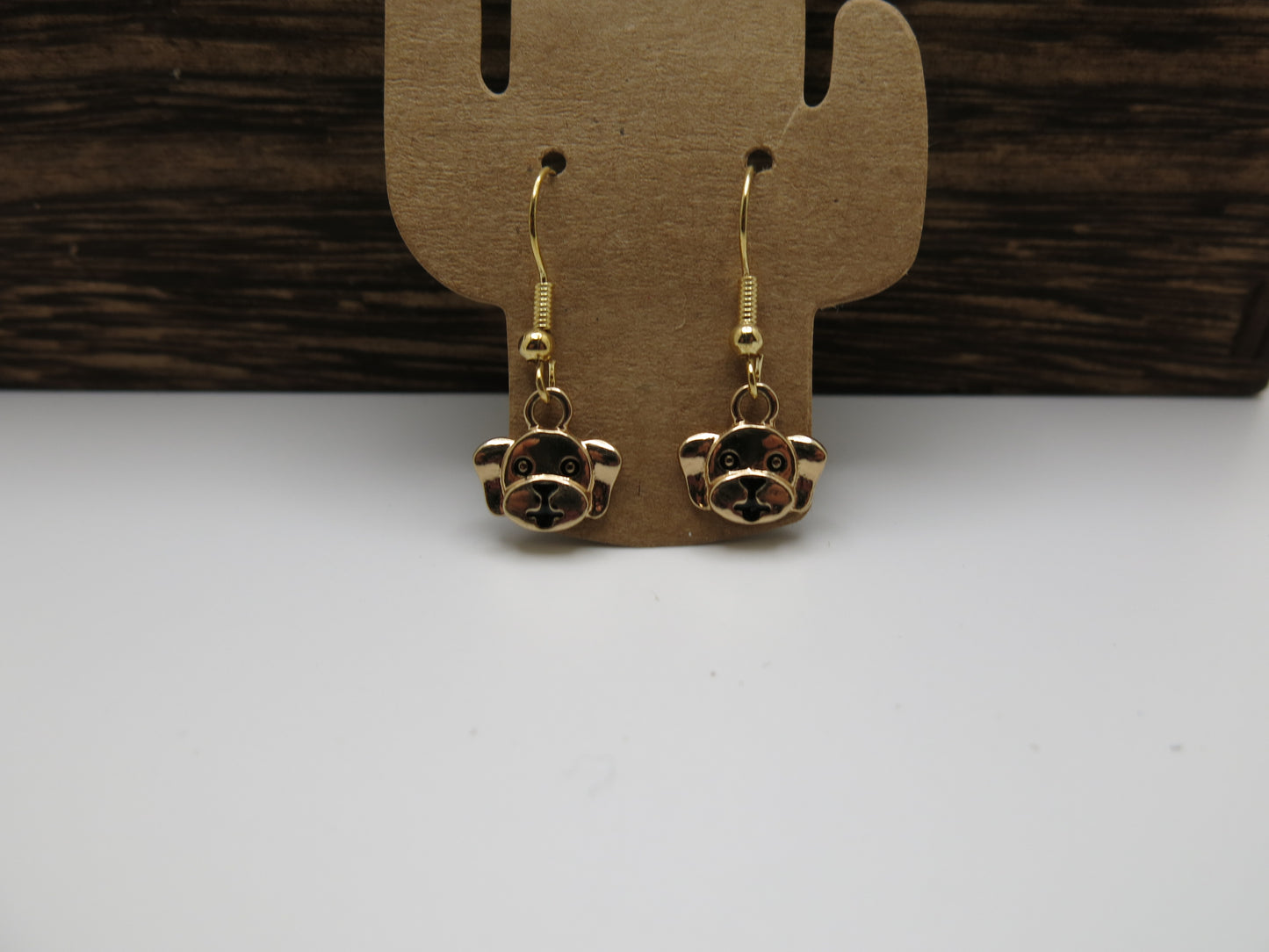 Gold dog-shaped earrings on a brown earring card with a wooden background