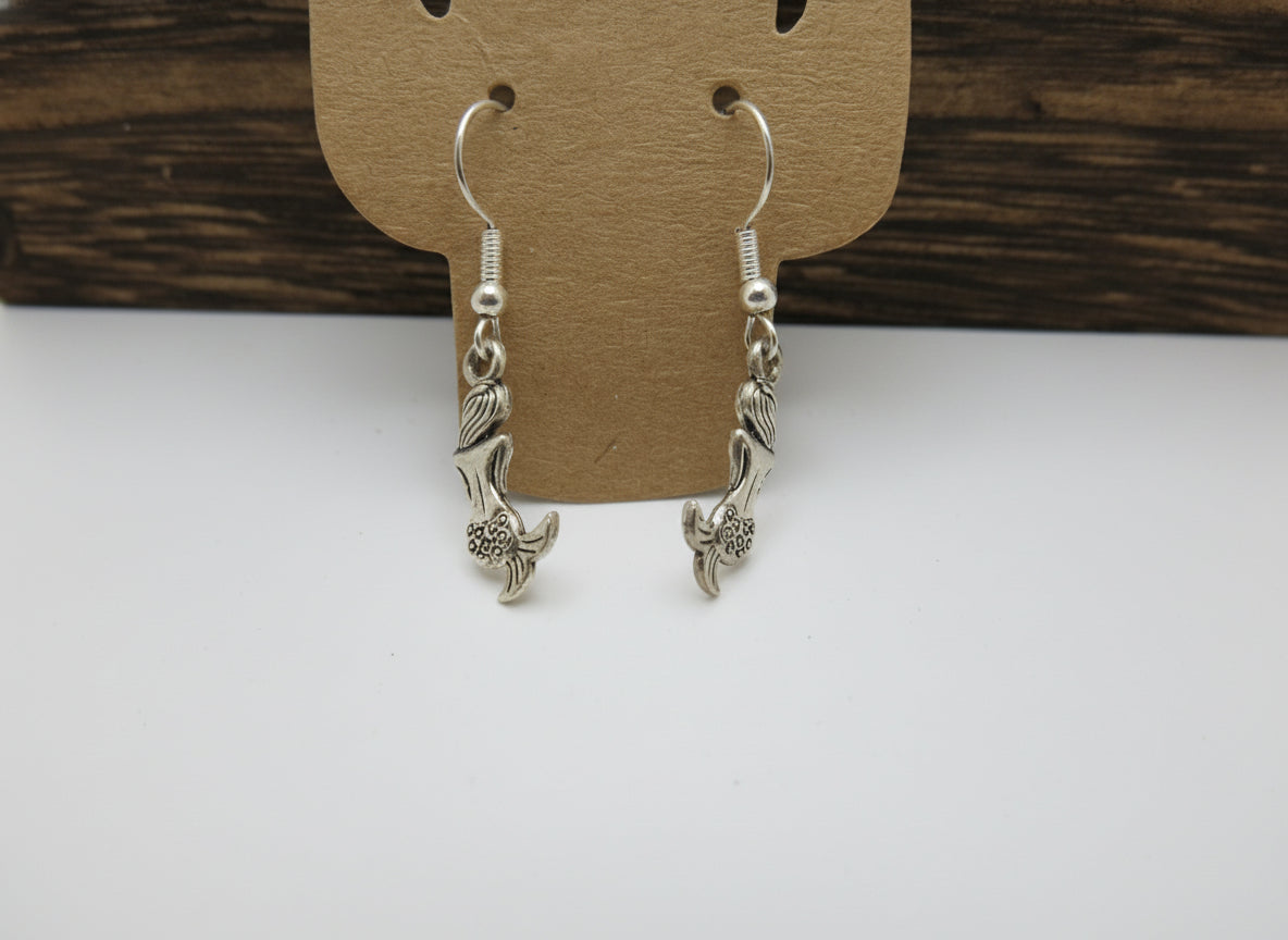 Silver earrings on a cardboard backing with a wooden surface in the background