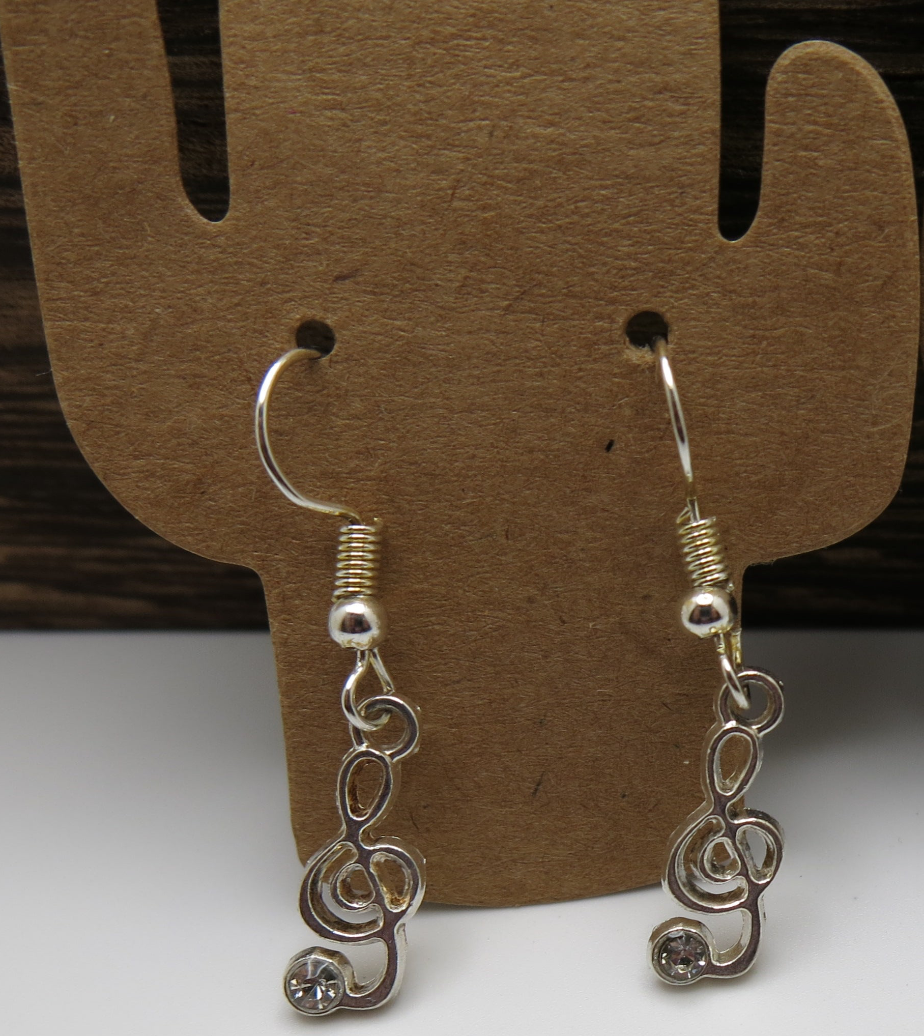 Silver treble clef earrings on a brown earring stand.