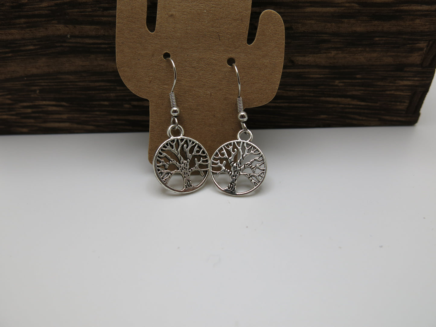 Silver tree-of-life earrings on a cactus-shaped card with a wooden background