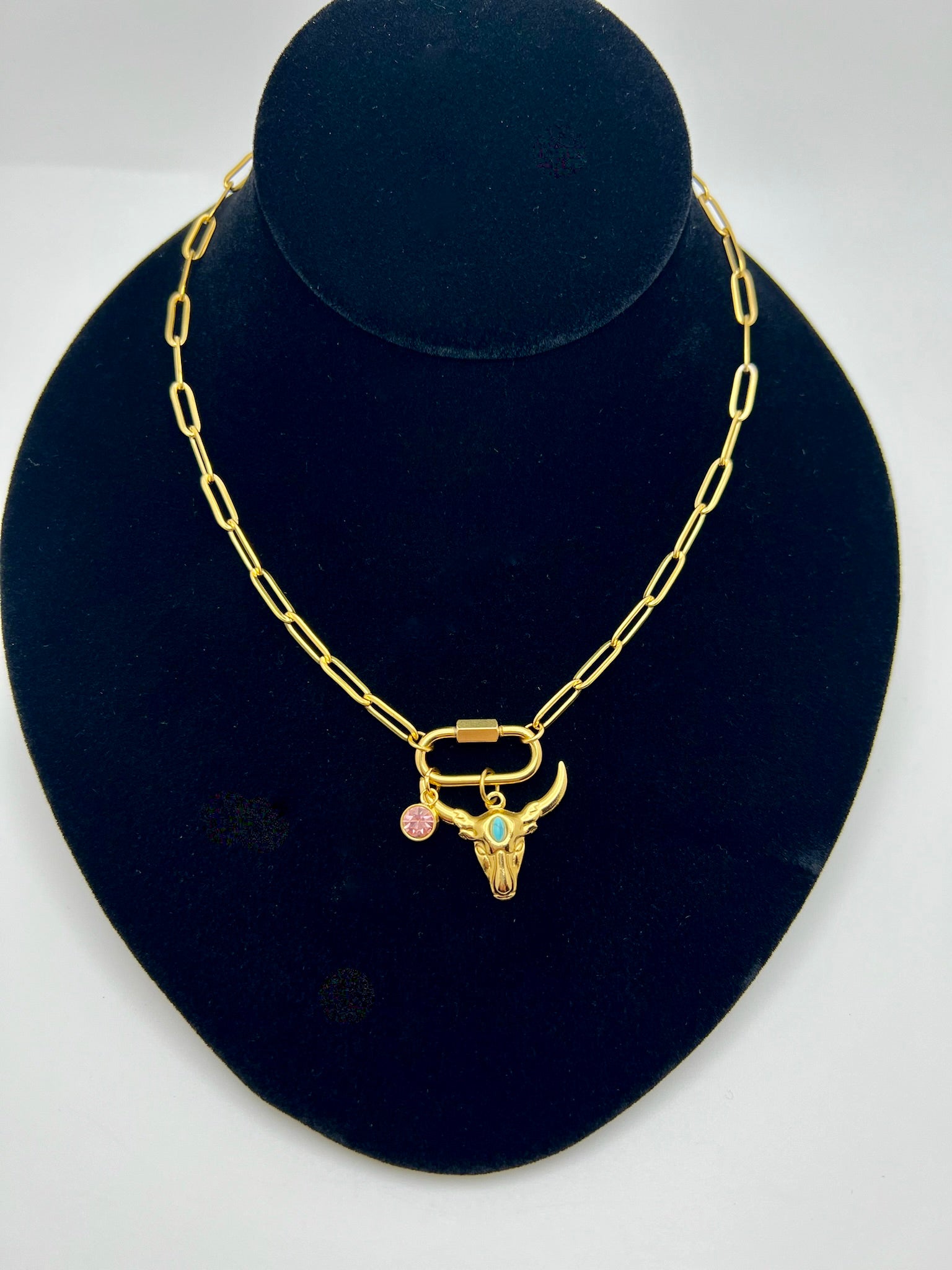 Gold necklace with a bull head pendant on a black velvet stand.