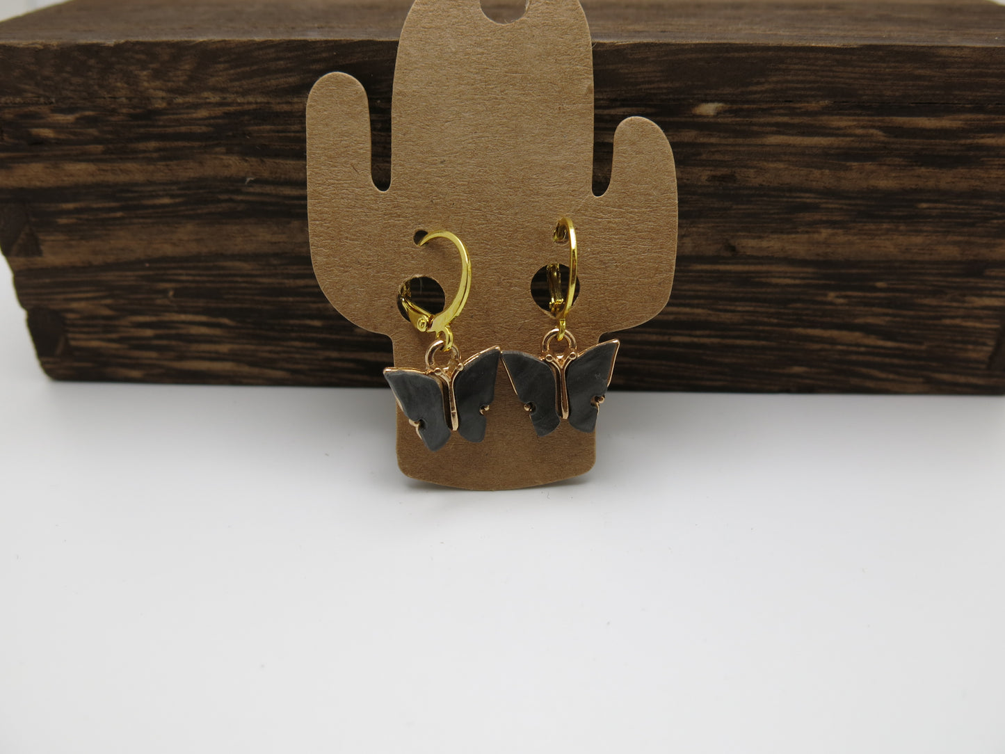 Butterfly-shaped earrings on a cactus-shaped stand against a wooden background