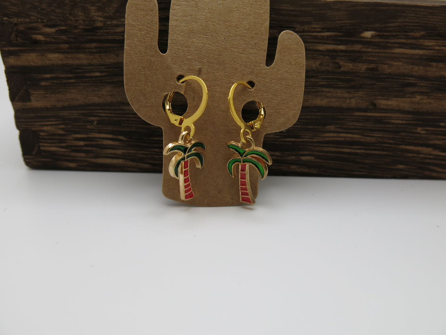 Palm tree earrings on a cactus-shaped earring stand against a wooden background