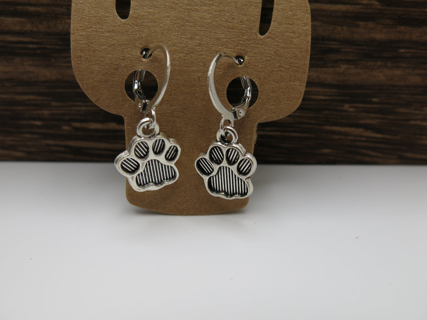 Silver paw print earrings on a wooden display card with a white background