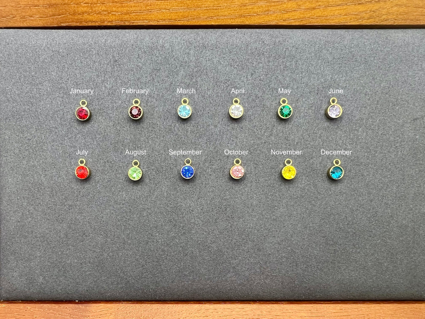 Set of twelve small colorful charms on a gray card with months labeled.