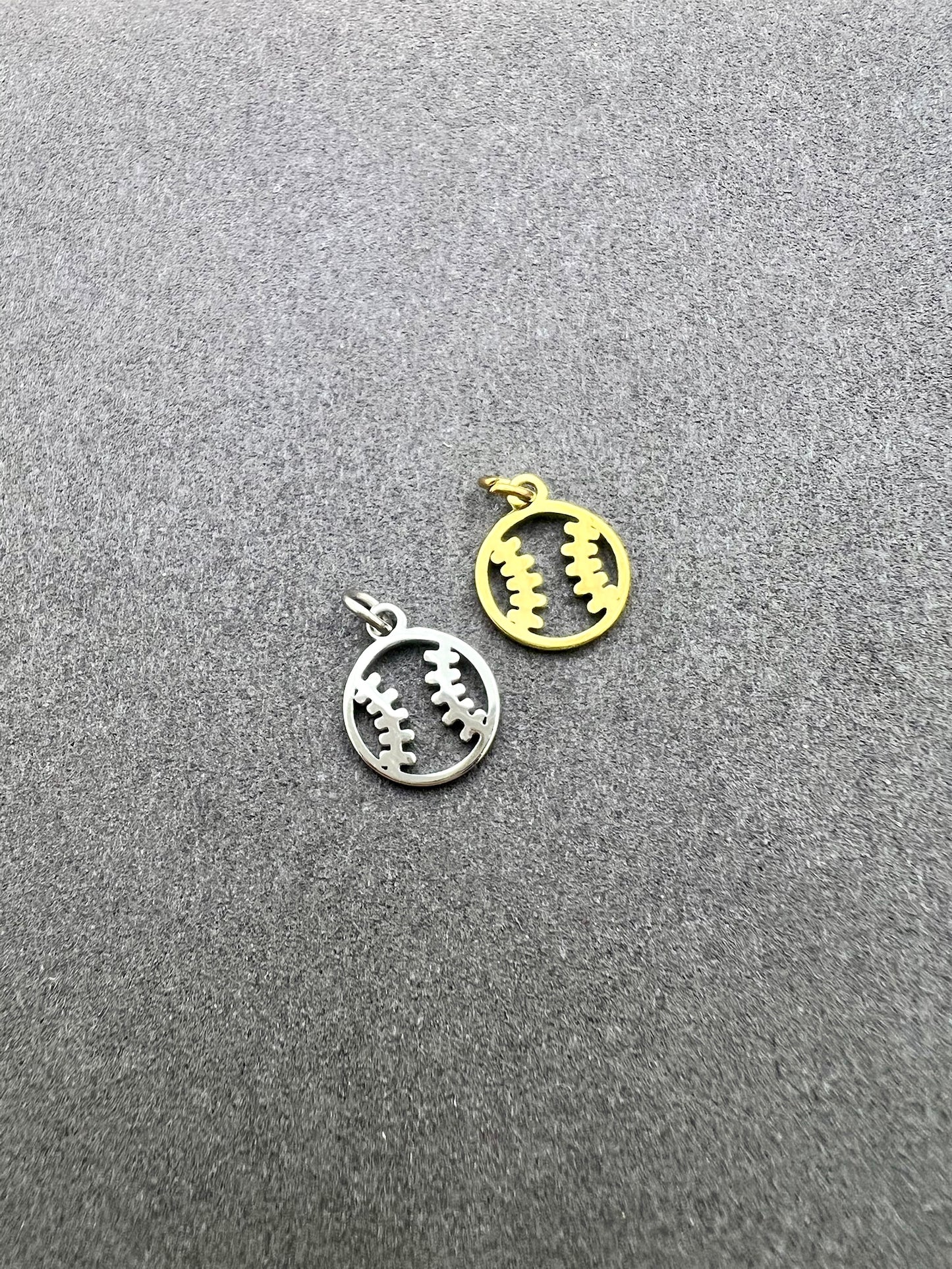 Two metal pendants, one silver and one gold, on a gray surface.