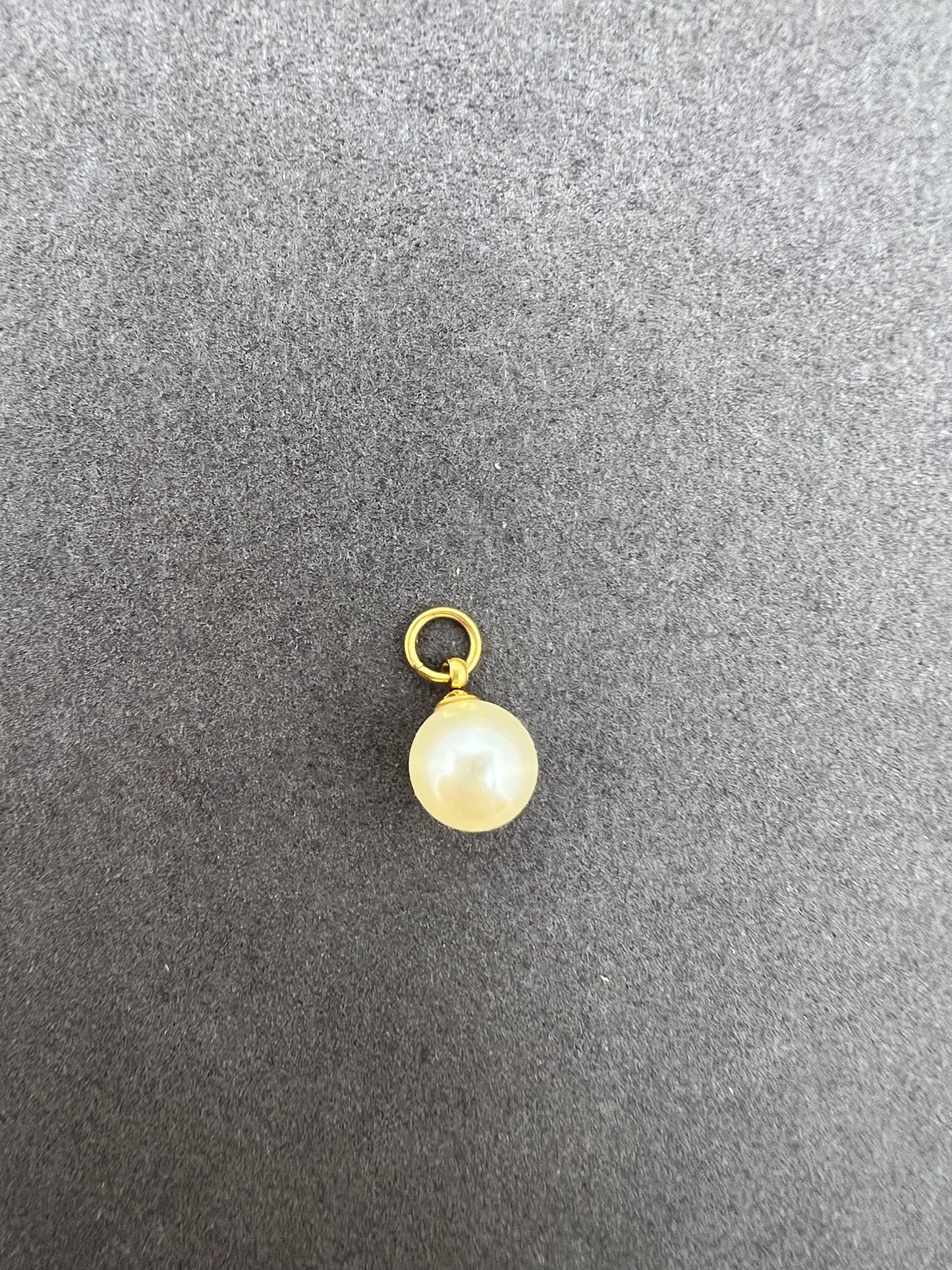 Gold pendant with a pearl on a gray background