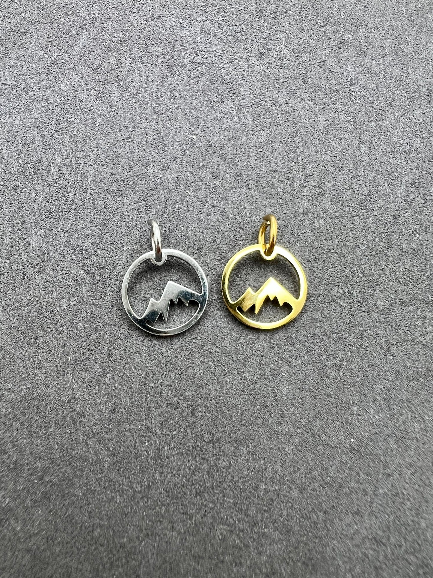 Two mountain-shaped pendants, one silver and one gold, on a gray surface.