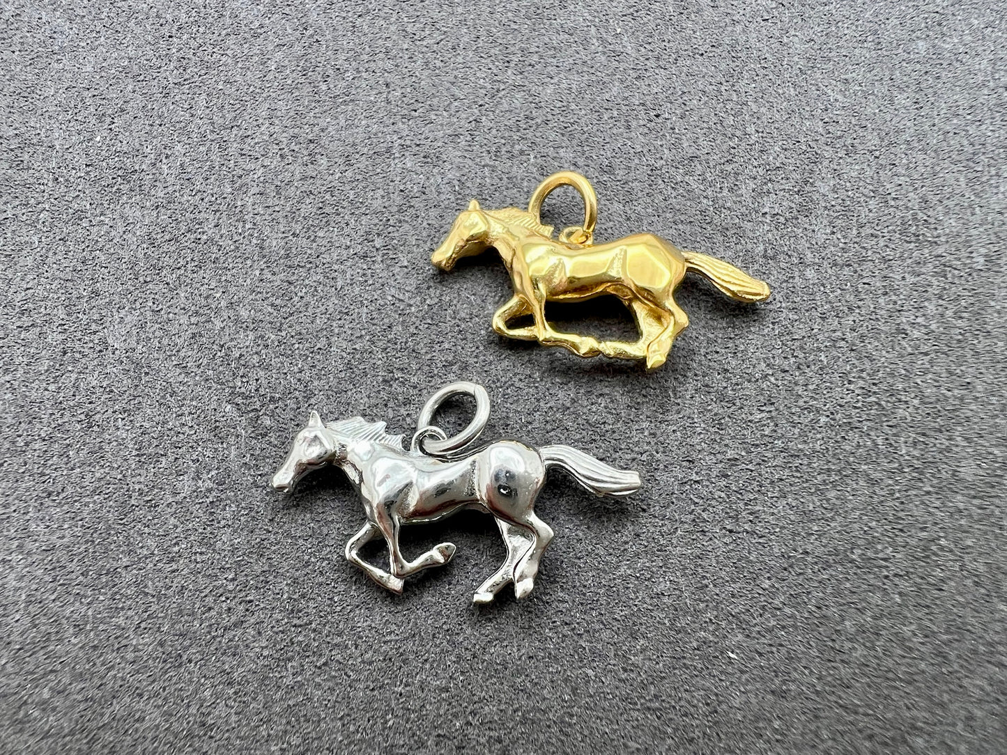Two horse-shaped charms, one gold and one silver, on a gray surface.