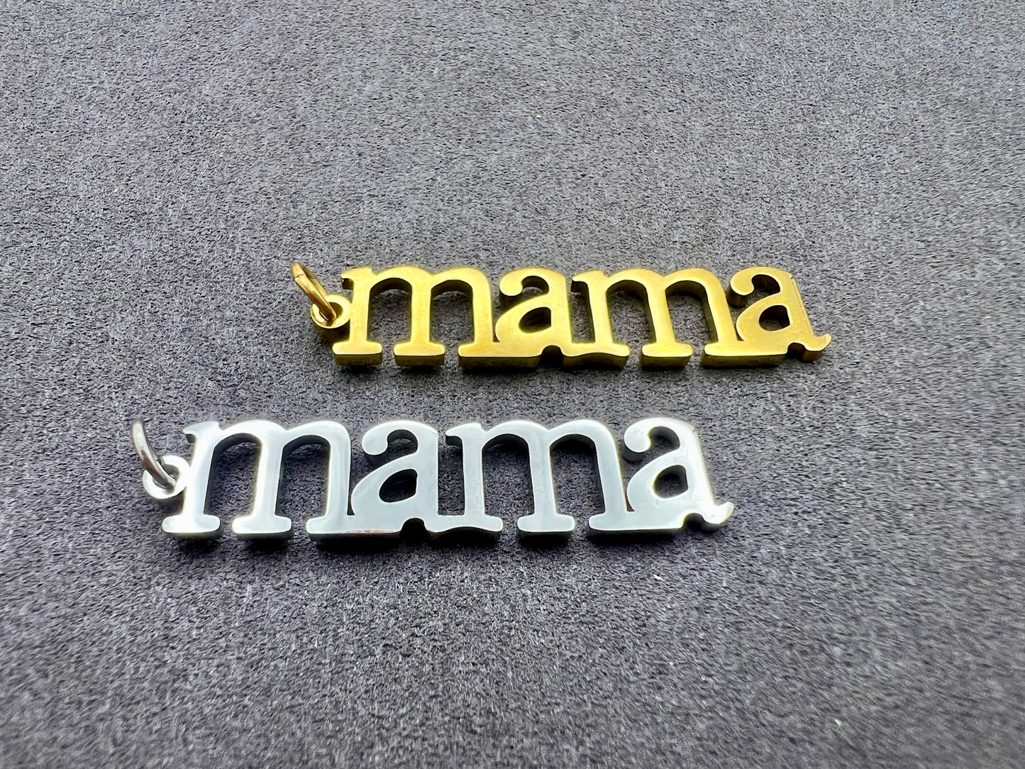 Two 'mama' pendants, one gold and one silver, on a gray background.