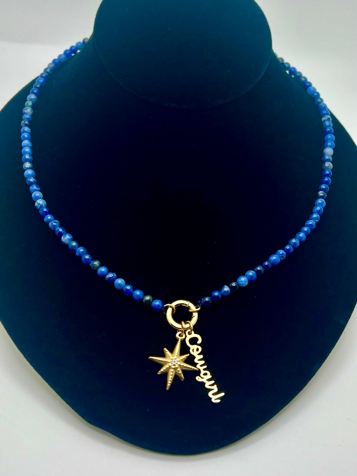 Blue beaded necklace with a gold starfish charm on a blue stand