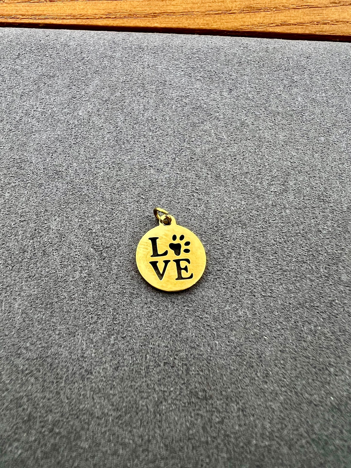 Gold pendant with 'LOVE' and paw print on a gray surface