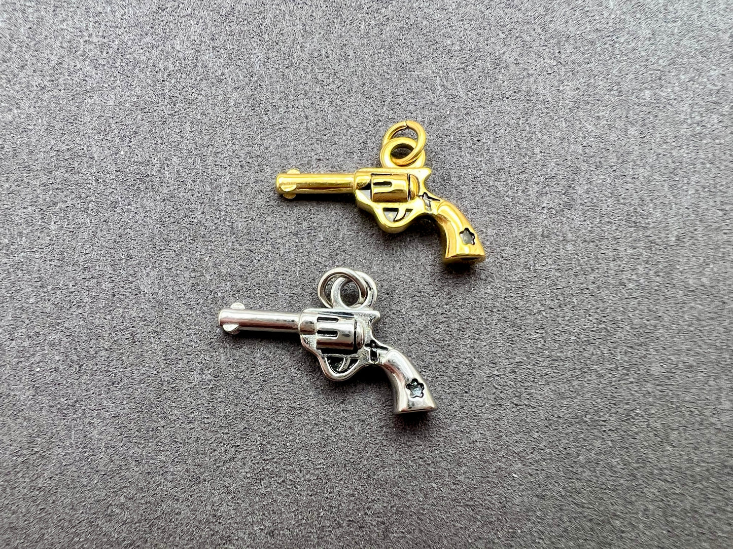 Two gun-shaped charms, one gold and one silver, on a gray background.
